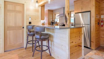 Un interior de madera con una isla de cocina, taburetes de bar, un refrigerador de acero inoxidable y armarios de madera.