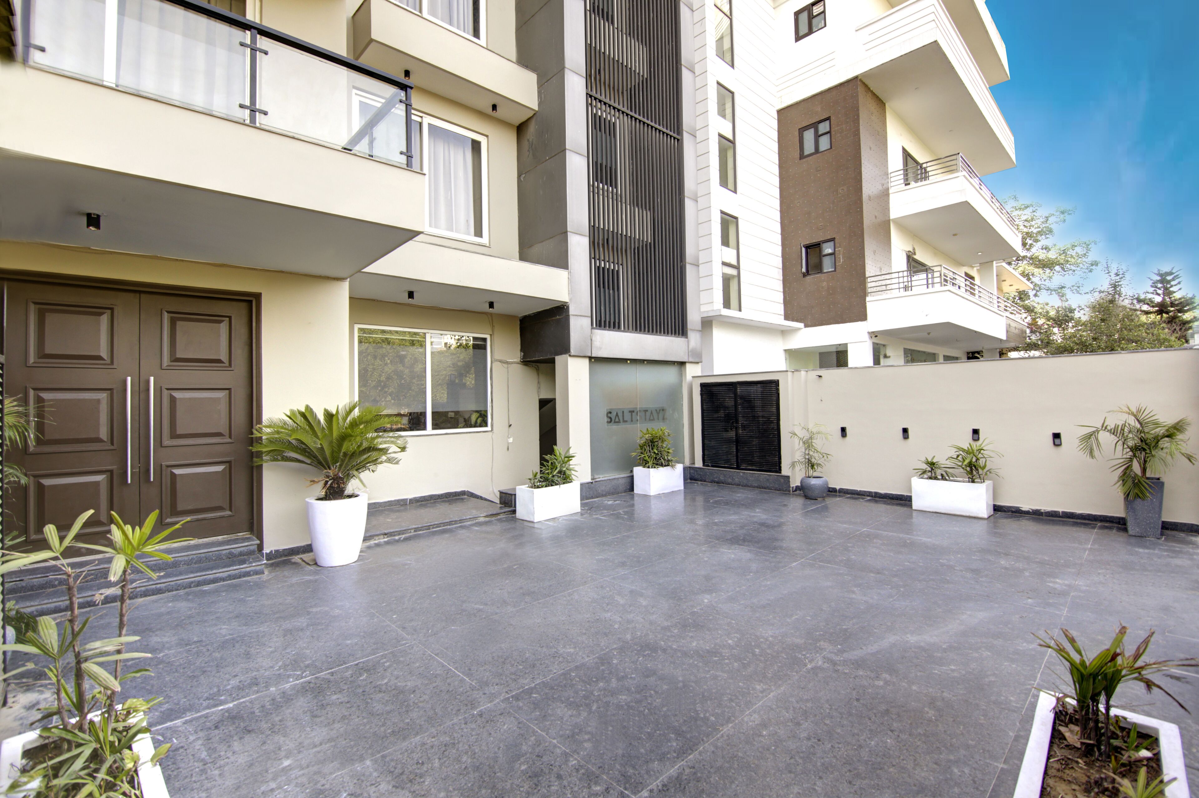 A modern building with a flat roof, multiple balconies, and a spacious courtyard with potted plants.