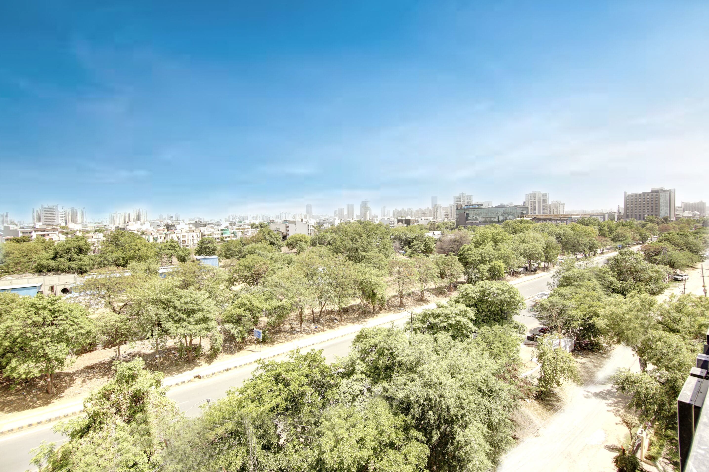 A cityscape with a clear sky, a road lined with trees, and buildings in the distance.