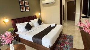 Habitación de hotel con una cama grande, una mesita de noche con un jarrón de flores, un aire acondicionado de pared y un televisor en la pared.