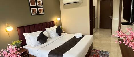 Habitación de hotel con una cama grande, una mesita de noche con un jarrón de flores, un aire acondicionado de pared y un televisor en la pared.
