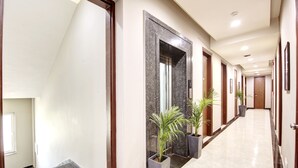 Un largo pasillo bien iluminado con suelo de mármol, puertas de madera y plantas en macetas.