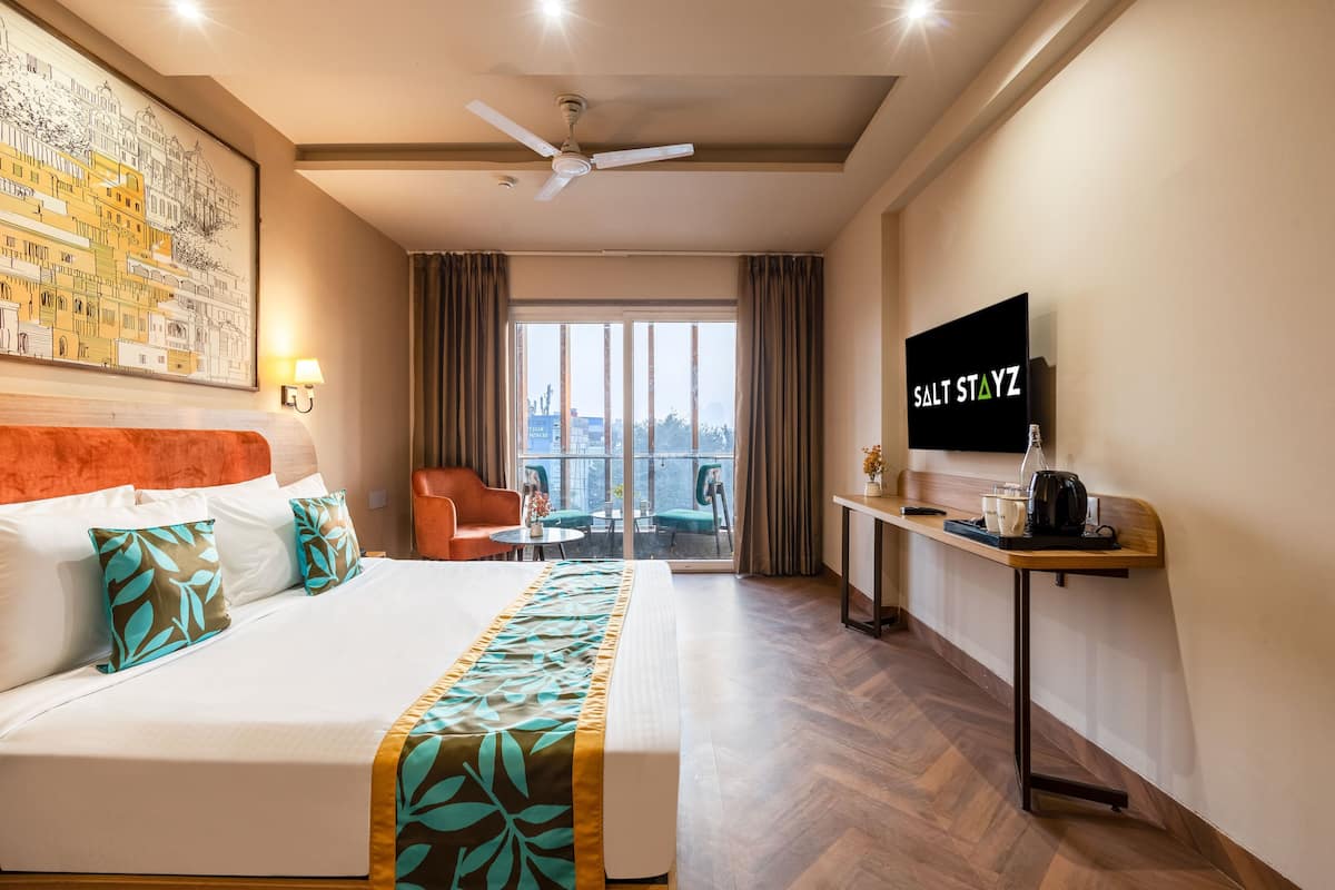 A hotel room with a bed, a desk, a chair, a TV, and a balcony with a city view.