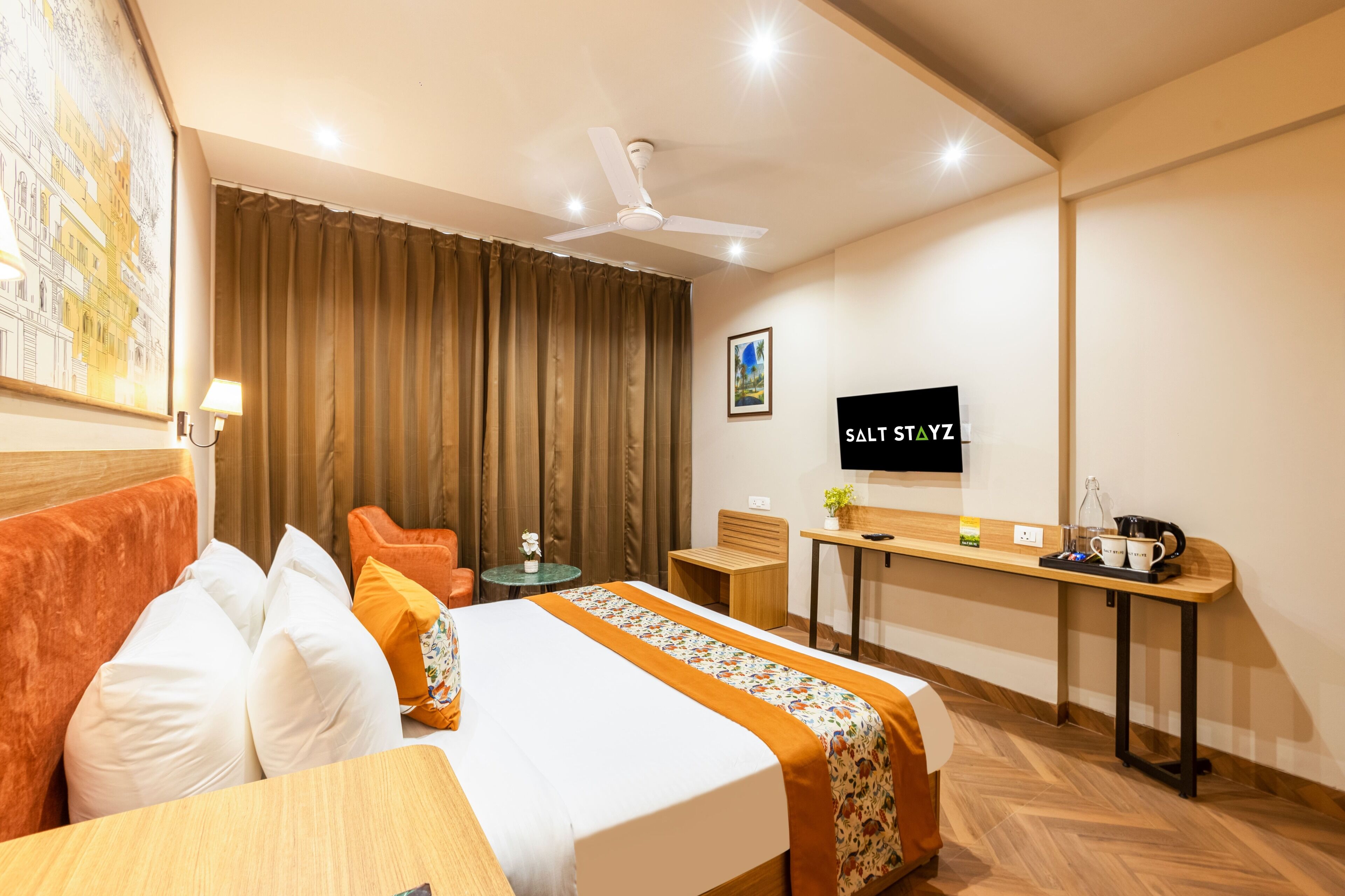 Una habitación de hotel con cama, escritorio, silla, televisor y ventilador de techo.