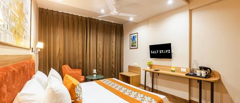 Una habitación de hotel con cama, escritorio, silla, televisor y ventilador de techo.
