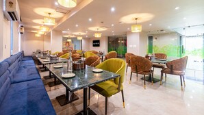 A modern restaurant with a long blue sofa, yellow and brown chairs, and a green wall. - Saltstayz Select- Medicity Near Medanta Hospital (Gurugram)