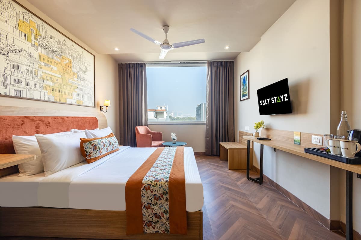A hotel room with a bed, a desk, a chair, a TV, and a window with a city view.