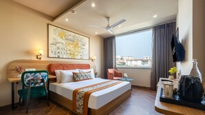 A hotel room with a bed, a desk with a chair, a television, a window with curtains, and a cityscape view. - Saltstayz Select- Medicity Near Medanta Hospital (Gurugram)
