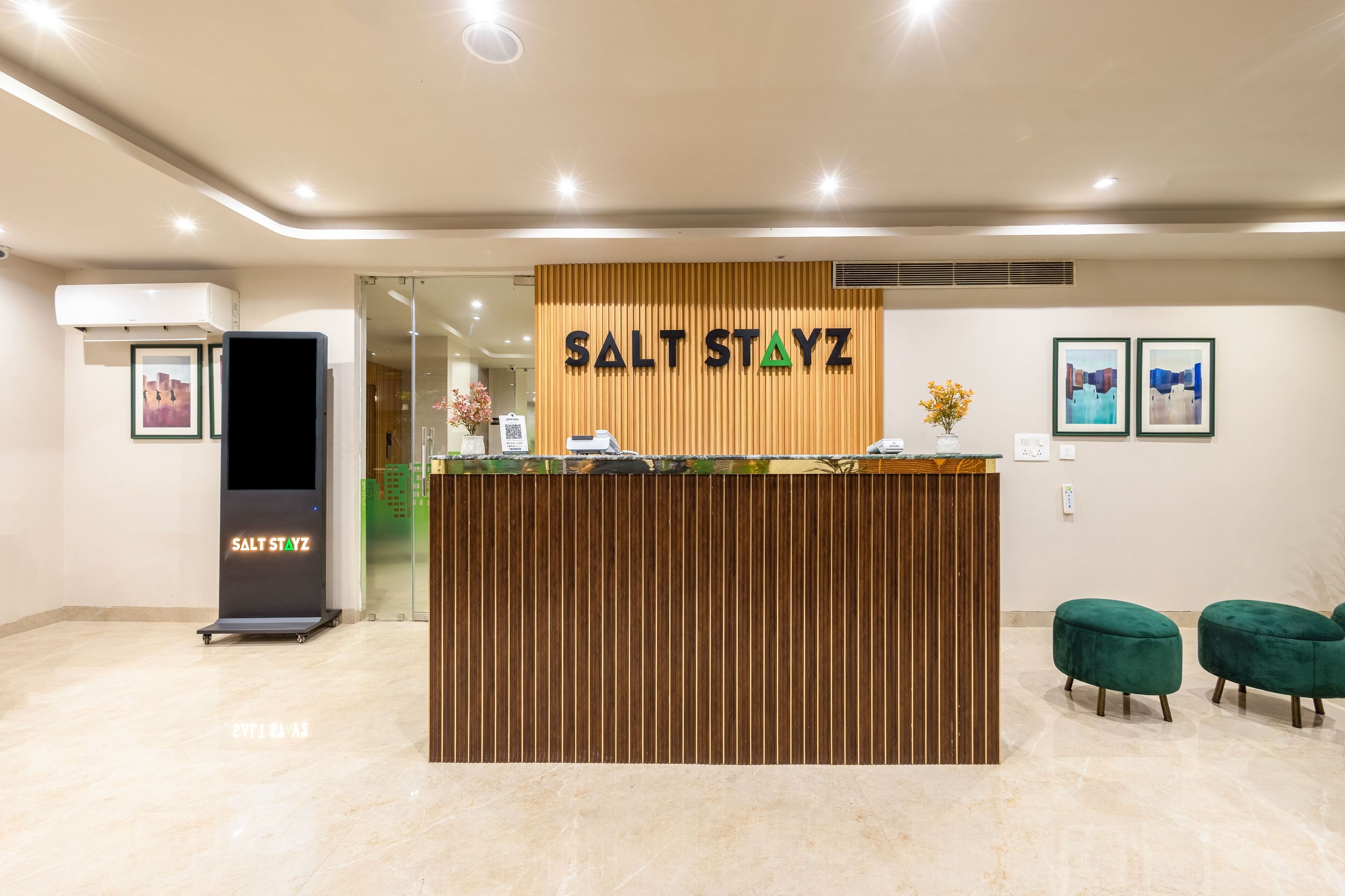 Un mostrador de recepción con diseño de paneles de madera, un letrero que dice "SALT STAYZ" y dos sillones tapizados en verde.