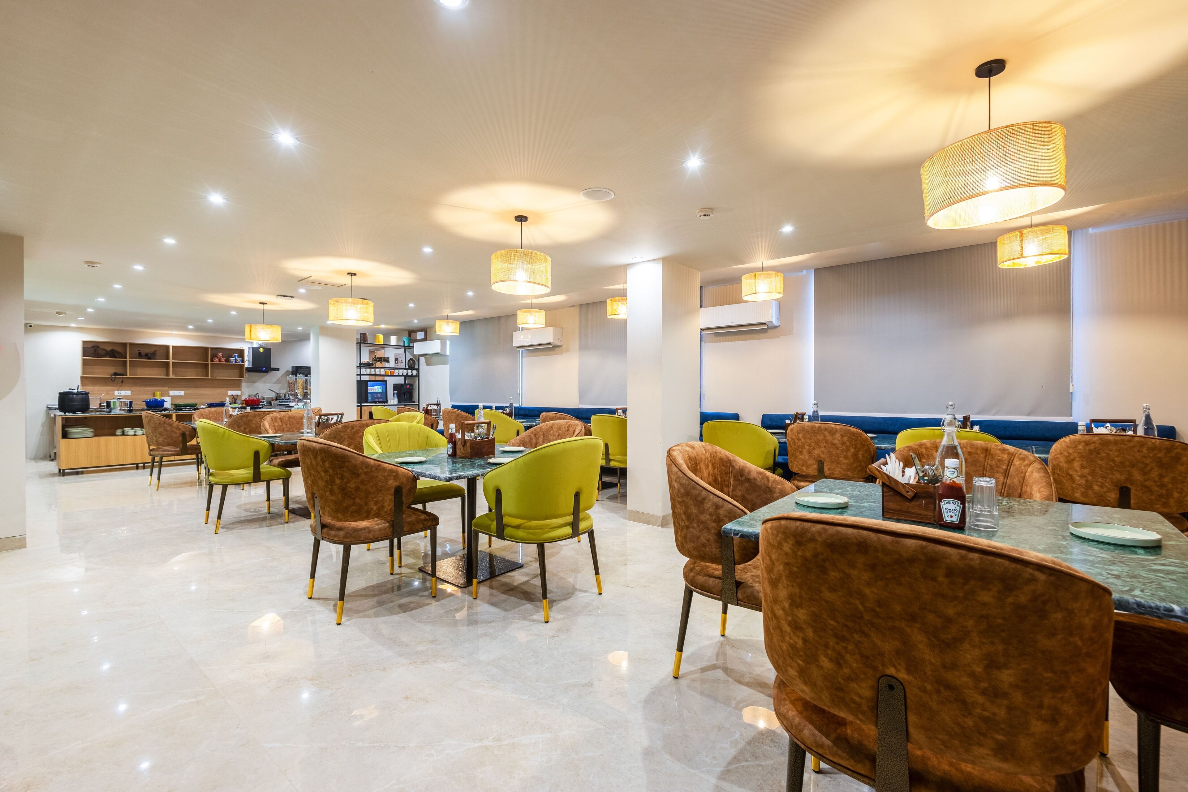 A modern dining area with multiple tables and chairs, overhead lighting, and a kitchen in the background.