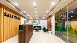 A reception area with a wooden wall, a reception desk, a green sofa, and framed pictures on the wall. - Saltstayz Select- Medicity Near Medanta Hospital (Gurugram)