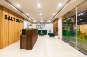 Zona de recepción con pared de madera, mostrador de recepción, sofá verde y cuadros enmarcados en la pared.