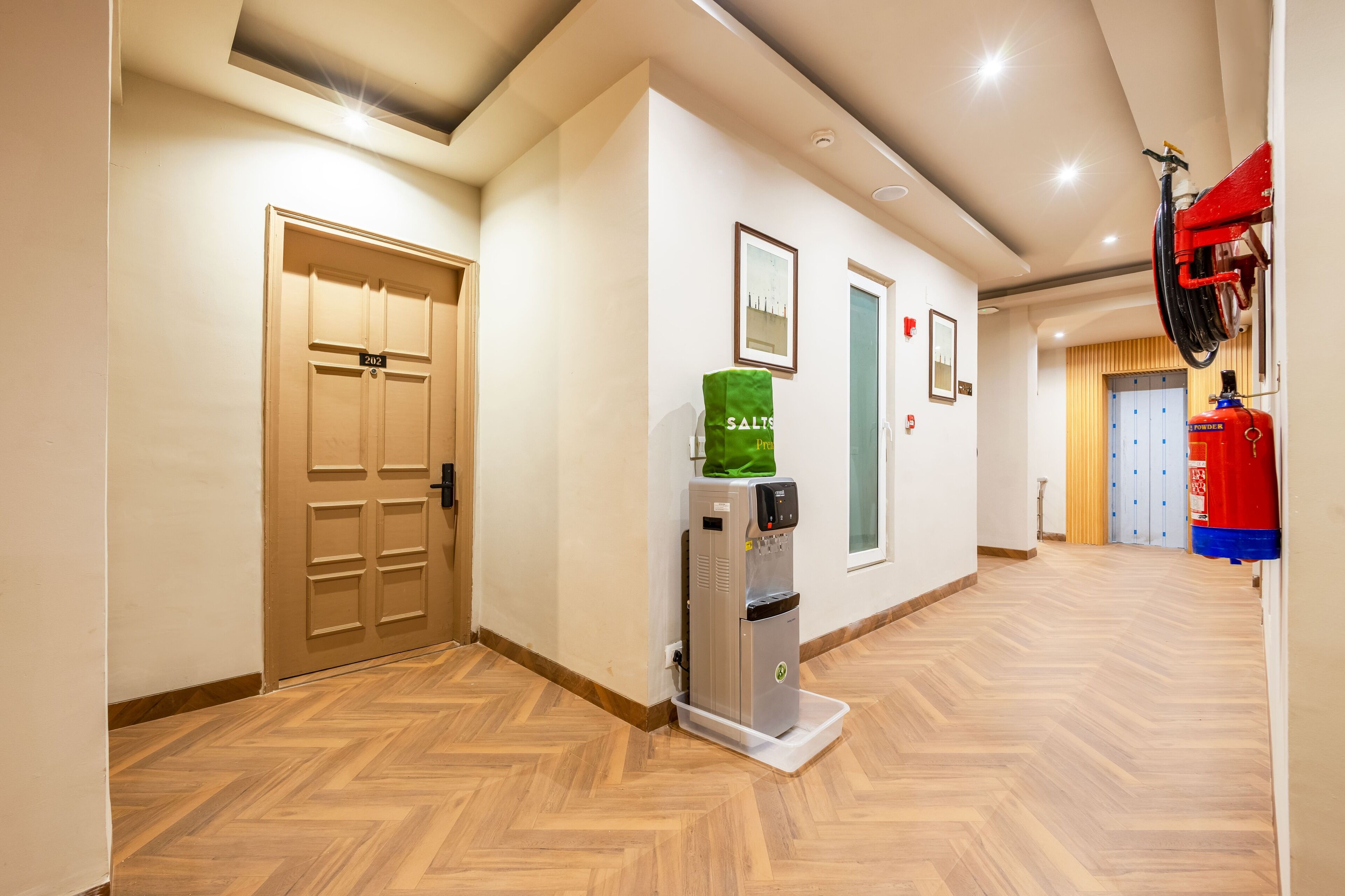 Corridoio di un hotel con pavimento in legno, un distributore d'acqua, un estintore e una porta con la scritta '212'.