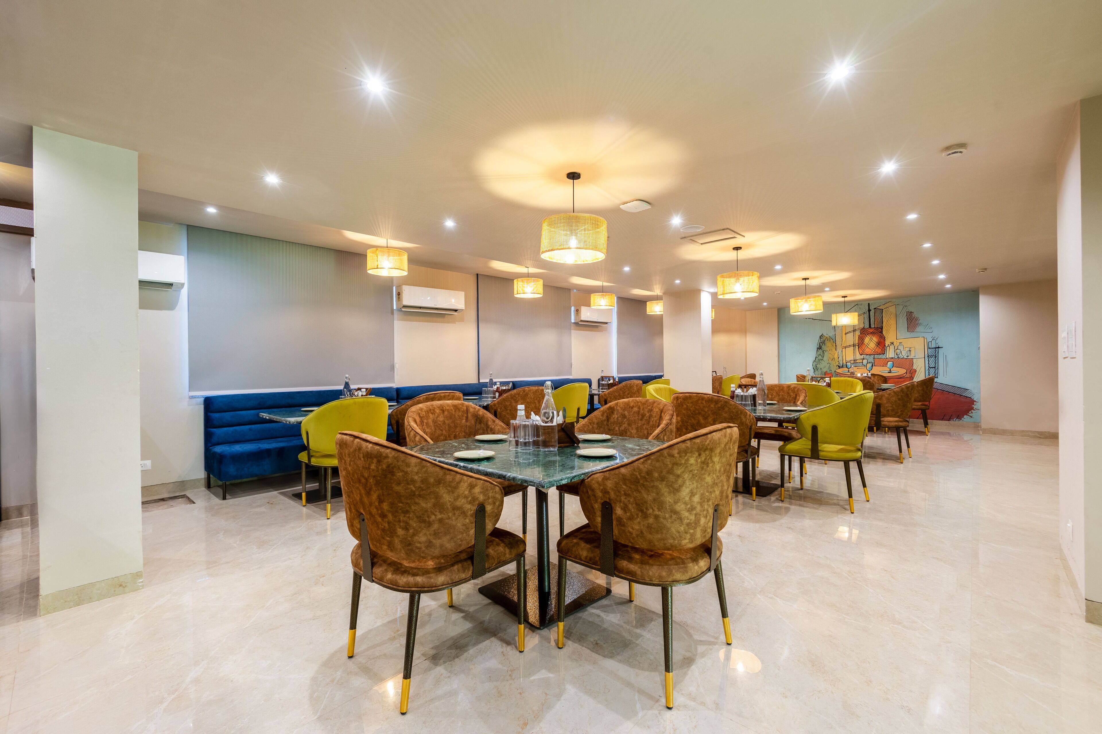 A spacious dining area with a large table and multiple chairs, a blue sofa, and a mural on the wall.