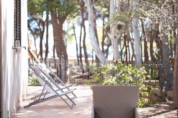 A sunlit outdoor area with a metal chair and a white wall.