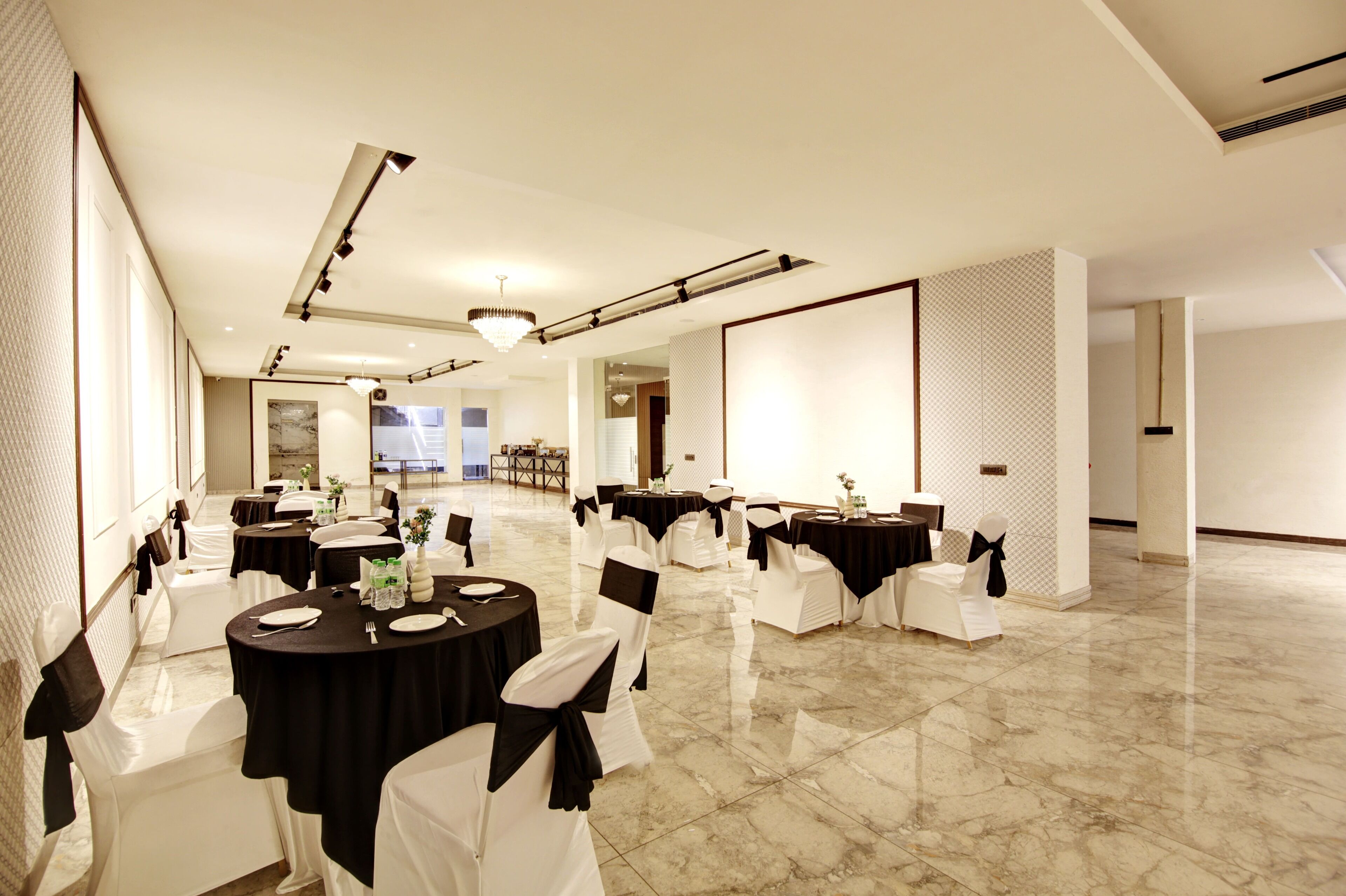 Une salle de banquet spacieuse, avec des tables rondes, des chaises blanches et des nappes noires.