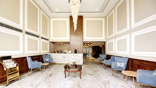 A spacious lobby with marble flooring, blue upholstered chairs, a central wooden coffee table, and a chandelier. - Saltstayz Premier – Cyber Hub (Gurugram)