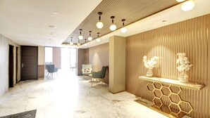 A modern hotel lobby with marble flooring, a reception desk with a honeycomb design, and a seating area with two chairs. - Saltstayz Premier – Cyber Hub (Gurugram)