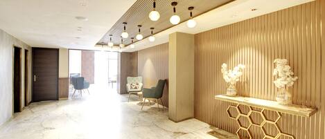 Un moderno vestíbulo de hotel con piso de mármol, un mostrador de recepción con diseño de panal y una zona de estar con dos sillones.