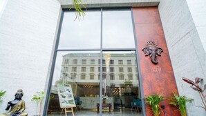 A modern building entrance with a glass door, a Buddha statue, and potted plants. - Saltstayz Premier – Cyber Hub (Gurugram)