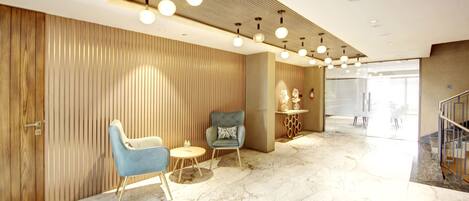 A modern lobby with a wooden panel wall, a blue armchair, a round table, and a marble floor.