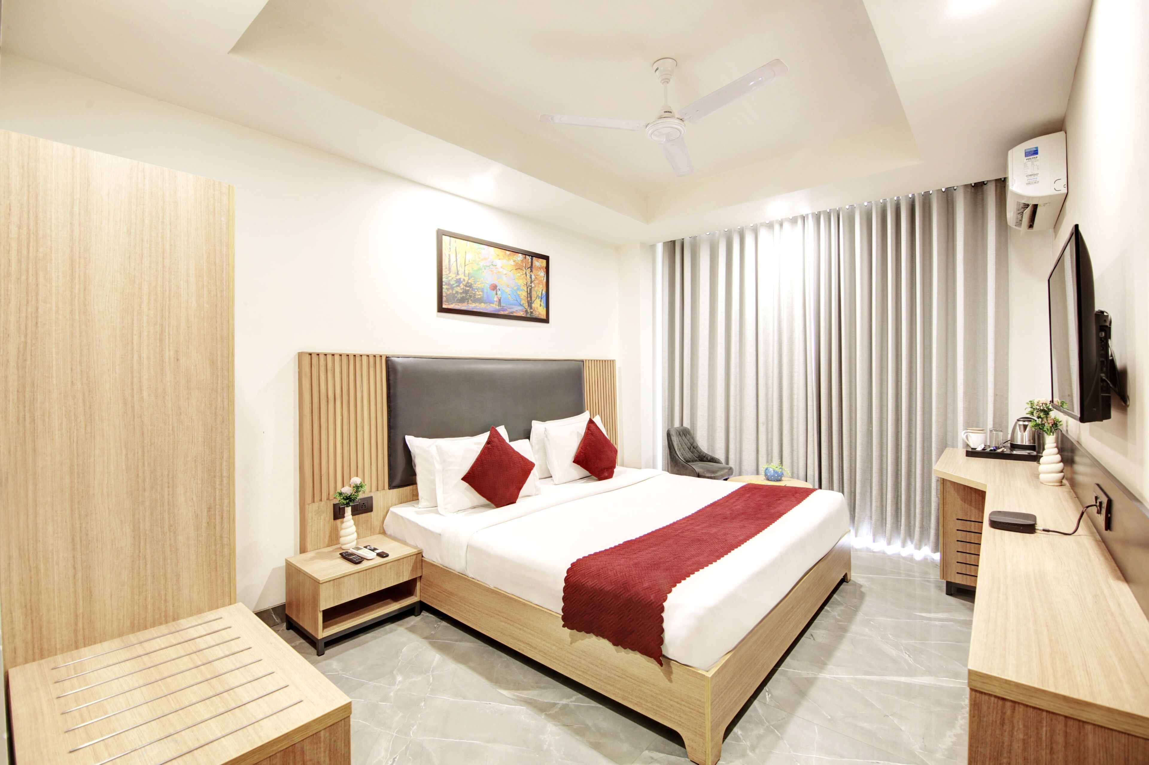A modern hotel room with a large bed, a desk, a chair, a TV, and a ceiling fan.