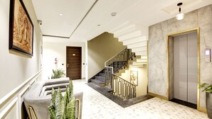 A modern hotel lobby with a marble staircase, a reception desk, and a large framed artwork on the wall. - Saltstayz Premier – Cyber Hub (Gurugram)