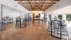 Un vaste espace dédié à la salle à manger, doté de hauts plafonds et de poutres apparentes, avec des tabourets de bar modernes et une table centrale agrémentée d'un vase de fleurs.