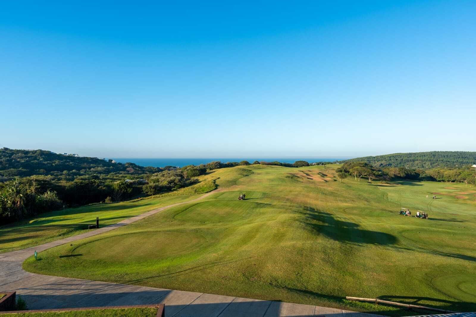 A golf course with a clear view of the fairway, sand bunkers, and a distant body of water.