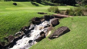 Un parcours de golf agrémenté d’un petit ruisseau, d’un pont en bois et d’une végétation luxuriante.
