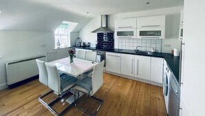 Een moderne keuken met witte kasten, een zwart aanrecht en een eethoek met een tafel en stoelen.