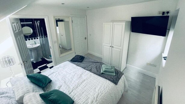 Een slaapkamer met een bed, een kledingkast, een televisie en een badkamer door een geopende deur zichtbaar.