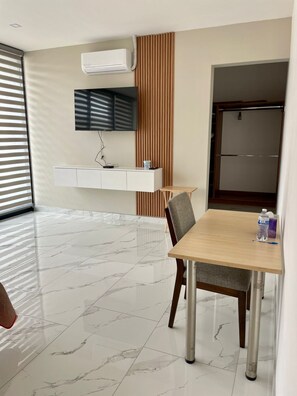 A modern dining area with a marble floor, a wooden table, and chairs. There is a white cabinet with a flat-screen TV mounted above it. - Casa Santacruz (Ensenada)
