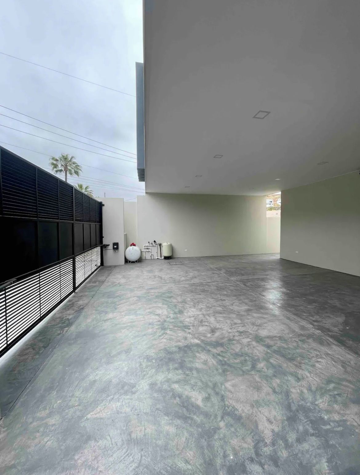 A spacious indoor area with a concrete floor, a black metal fence, and a white wall with a window.