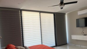 A modern bedroom with a bed, a ceiling fan, and large windows with blinds. - Casa Santacruz (Ensenada)