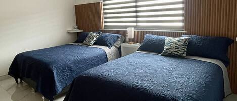 A bedroom with two beds, a ceiling fan, an air conditioning unit, and a window with blinds.