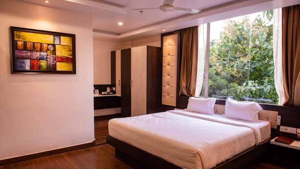 A modern bedroom with a large bed, a wardrobe, a vanity, and a window with curtains. - WELCOME SPA & RESORTS (Sambalpur)