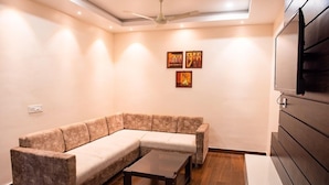 A modern living room with a sectional sofa, a coffee table, and a flat-screen TV mounted on the wall. - WELCOME SPA & RESORTS (Sambalpur)