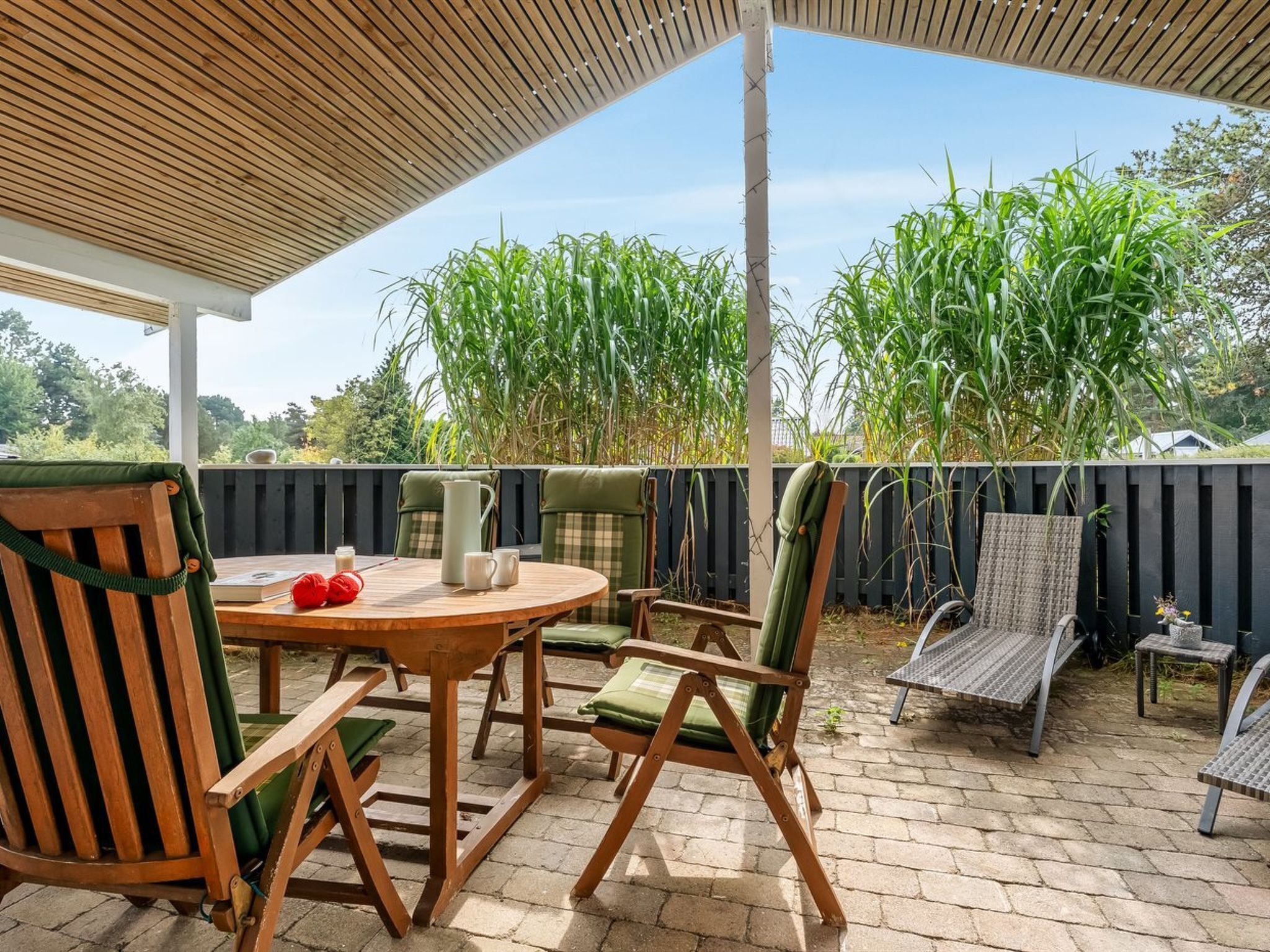 Een overdekt terras met een houten tafel en stoelen, een waterkan en een boek.