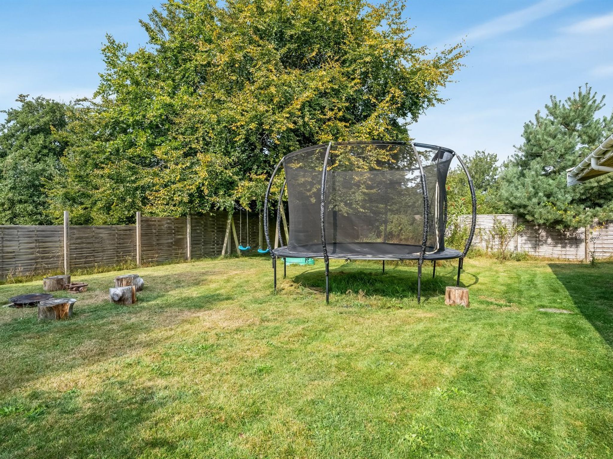 A backyard with a trampoline, a swing set, and a wooden fence.