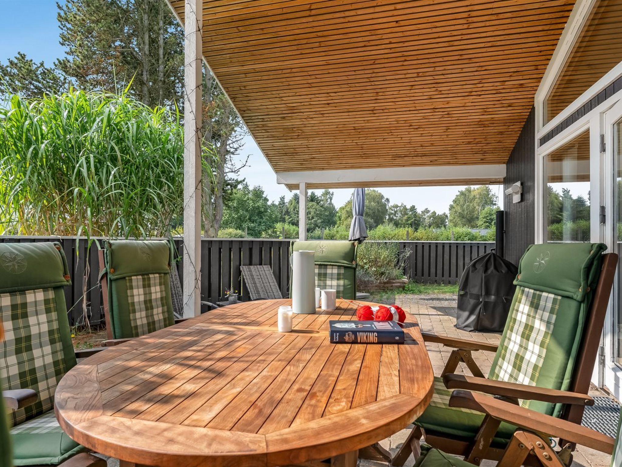 A wooden table with chairs, a book, and a grill in a covered outdoor area.