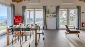 Une salle à manger spacieuse avec une table dressée pour six personnes, une cuisine dotée d’un réfrigérateur rouge et une vue sur l’extérieur.