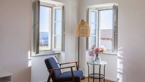 Une pièce avec deux fenêtres, une chaise, une table ornée d’un vase de fleurs et un luminaire suspendu.