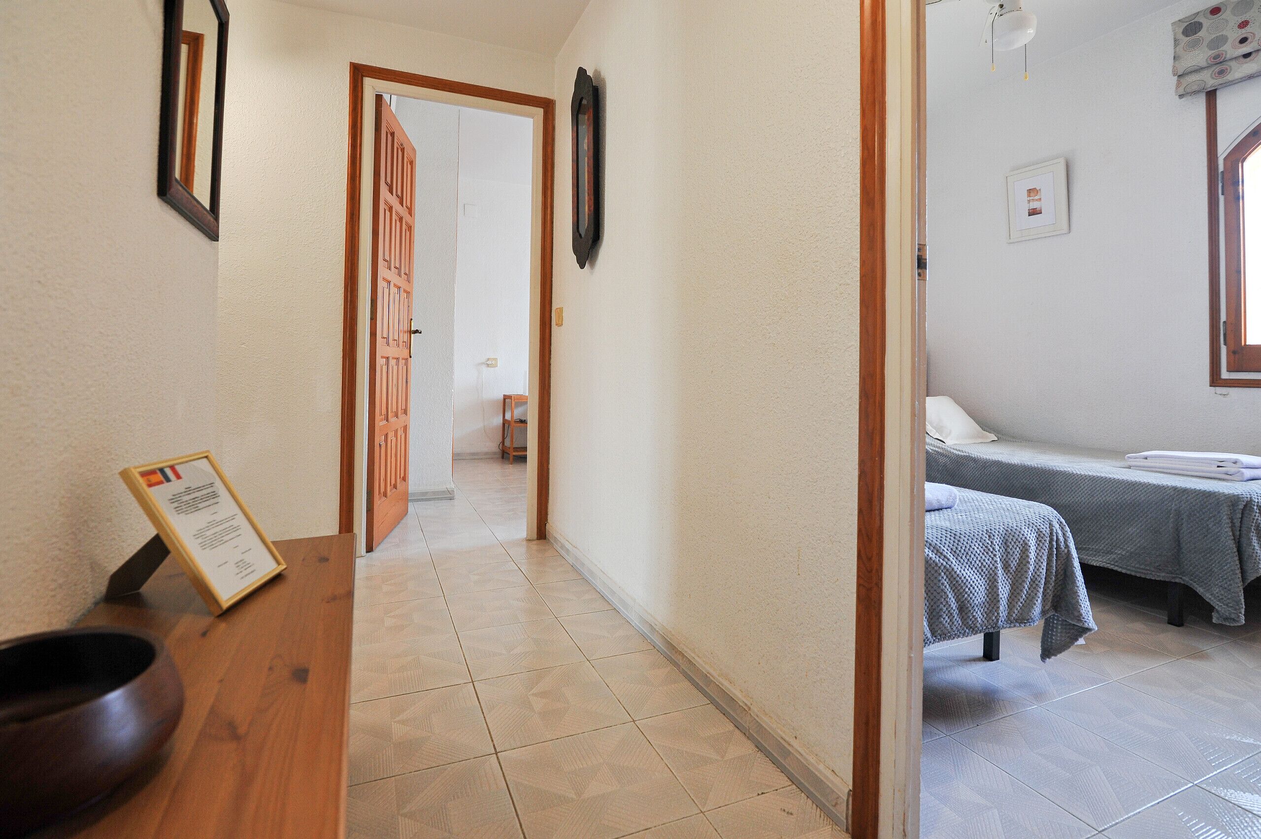 A hallway leading to a room with a bed, a wooden table with a sign, and a door.