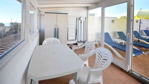 A covered outdoor area with a table and chairs, a view of the beach, and blue lounge chairs.