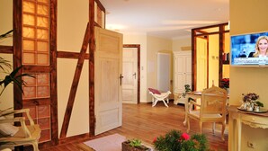 A room with a wooden floor, a white door, a white chair, a small table with a vase, and a television on the wall. - Apartment 'Wohnung 'am Kütertor' - Störtebeker' with Private Terrace and Wi-Fi (Stralsund)
