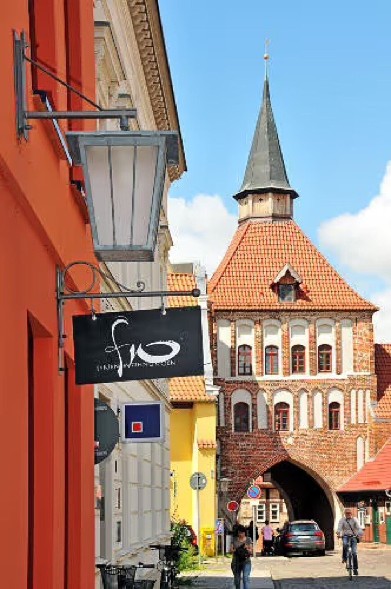 A street with a church, a red building, and a sign with a white logo.