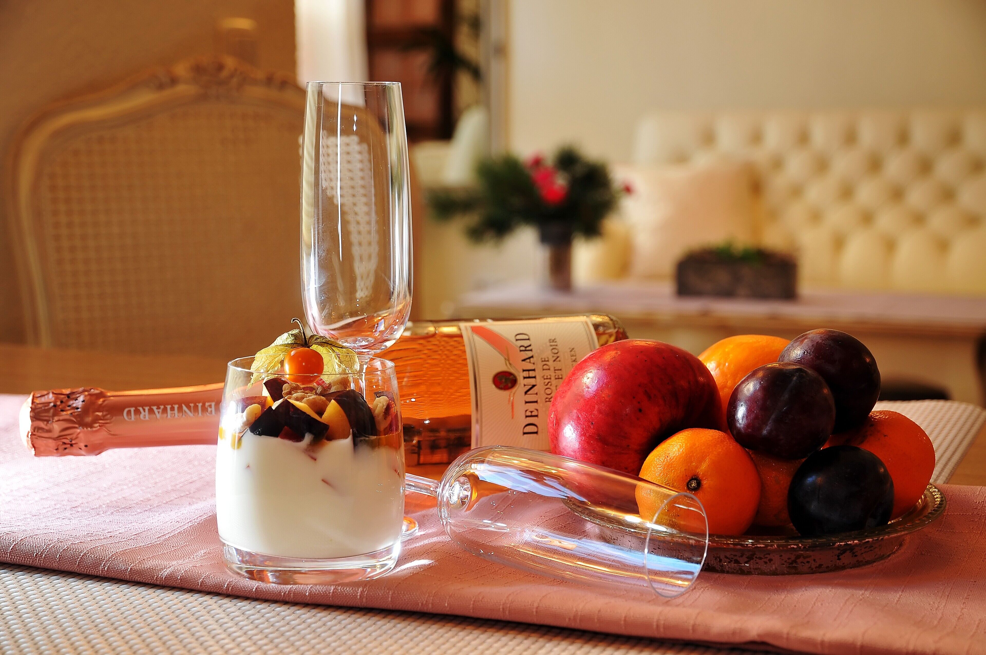 Une table avec une bouteille de champagne, un verre de vin doux et un saladier de fruits.