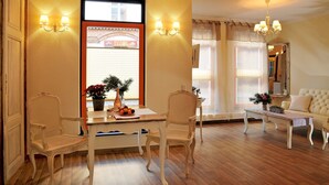 A room with a dining table, two chairs, a sofa, a chandelier, and a window with a view of a building. - Apartment 'Wohnung 'am Kütertor' - Störtebeker' with Private Terrace and Wi-Fi (Stralsund)