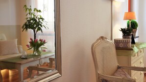 A room with a rattan chair, a small table with a vase of flowers, a lamp, and a television on the wall. - Apartment 'Wohnungen 'am Kütertor' - Kogge' with Balcony and Wi-Fi (Stralsund)